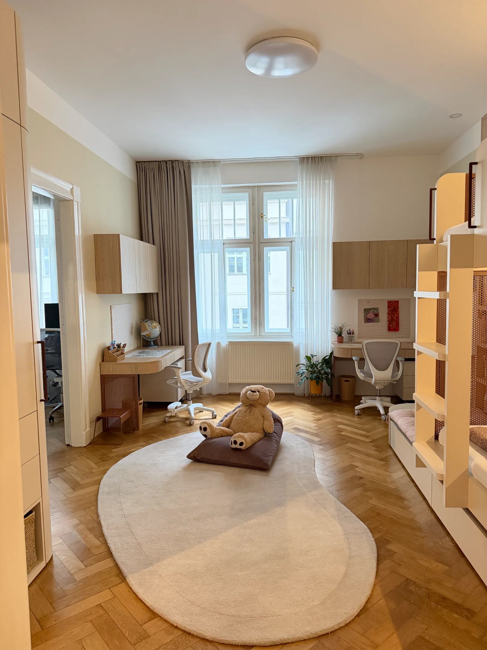 Dětský pokoj s psacími stoly, postelí a hračkami.